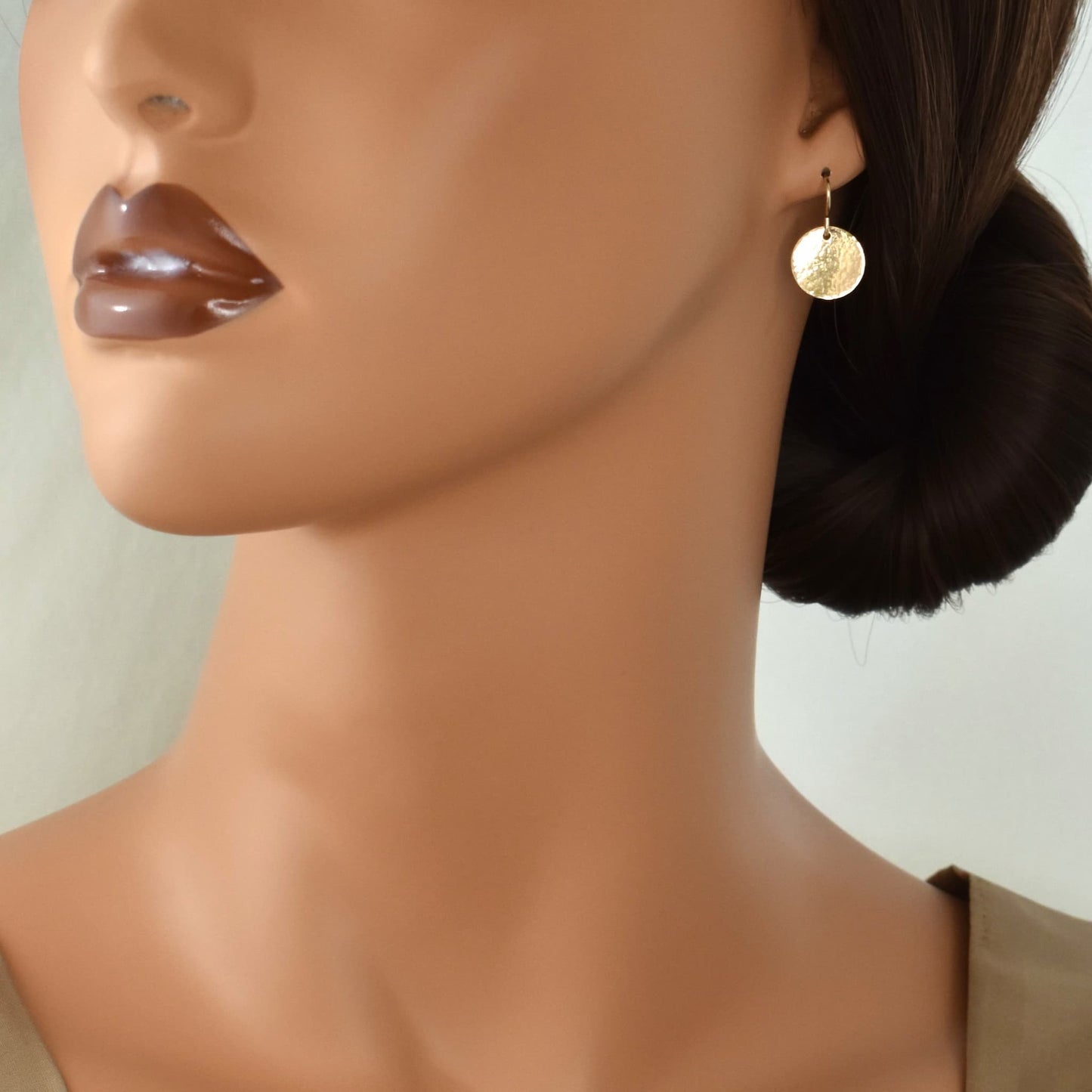 Gold circle drop earrings with hammered surface shown on model.