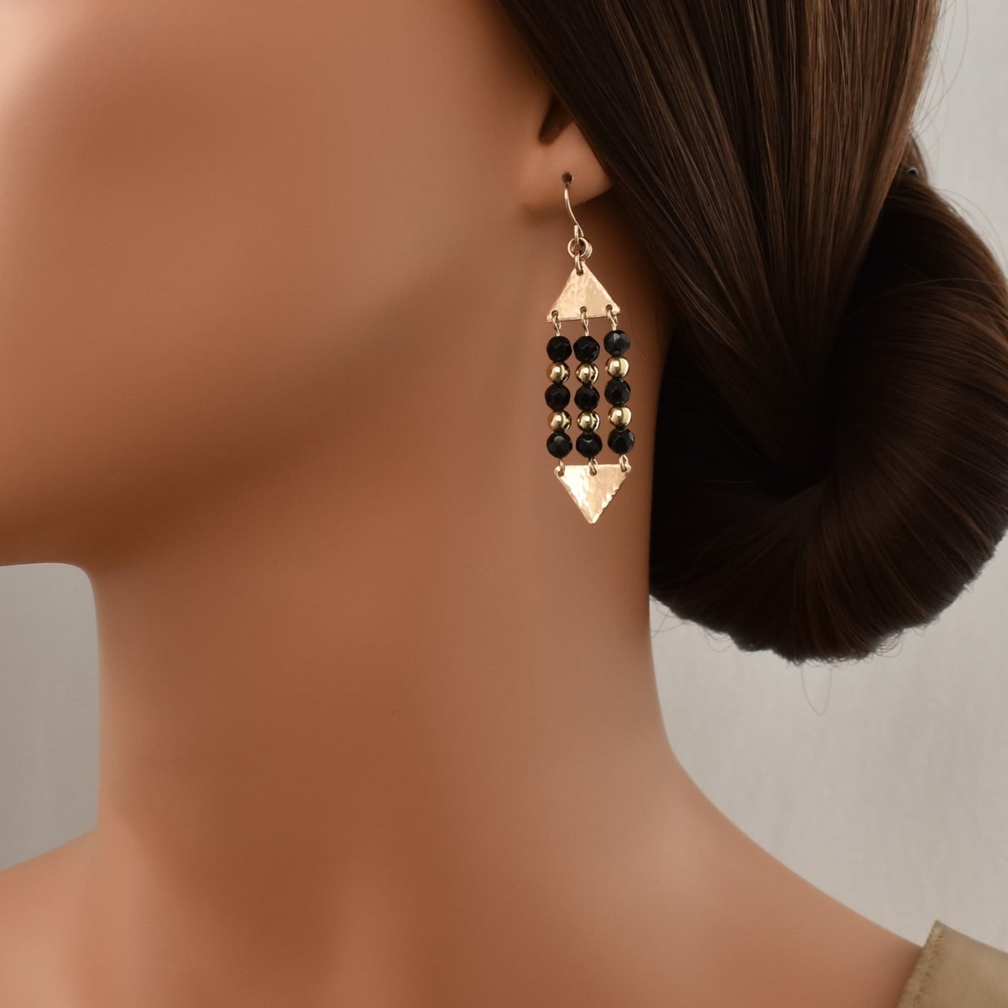 Gold triangle dangle earrings with black onyx gemstones shown on model.