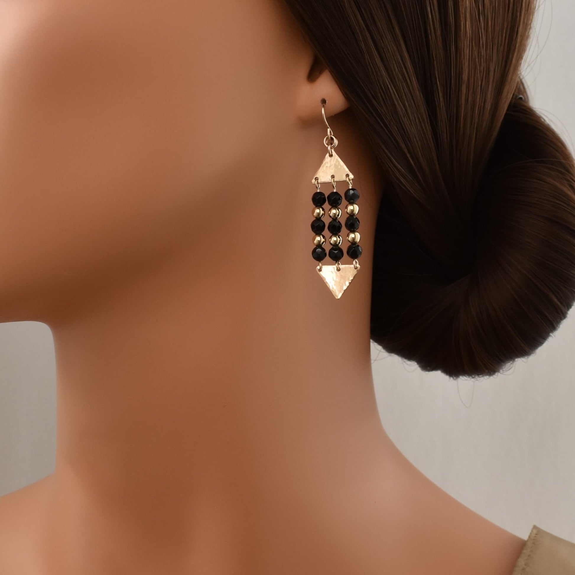 Gold triangle dangle earrings with black onyx gemstones shown on model.