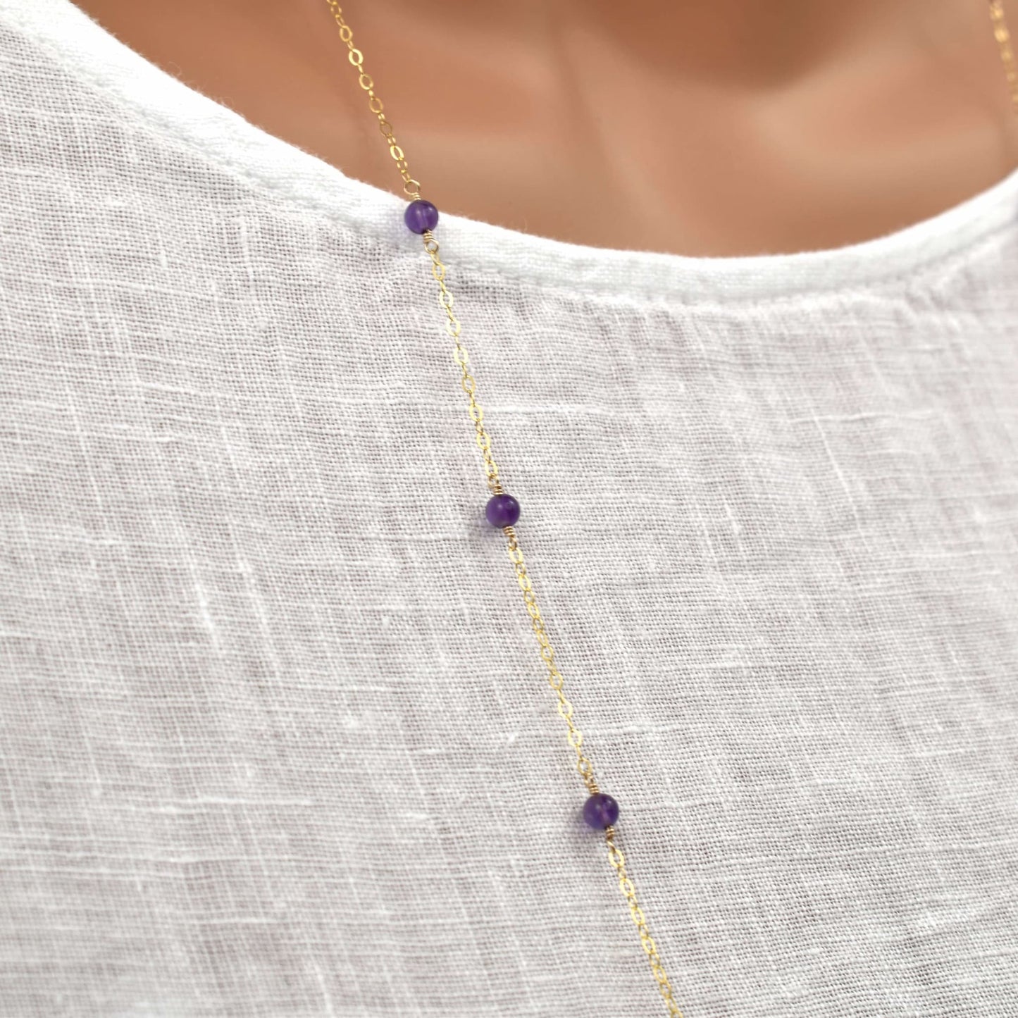 long gold necklace with dark purple amethyst beads shown in close up.